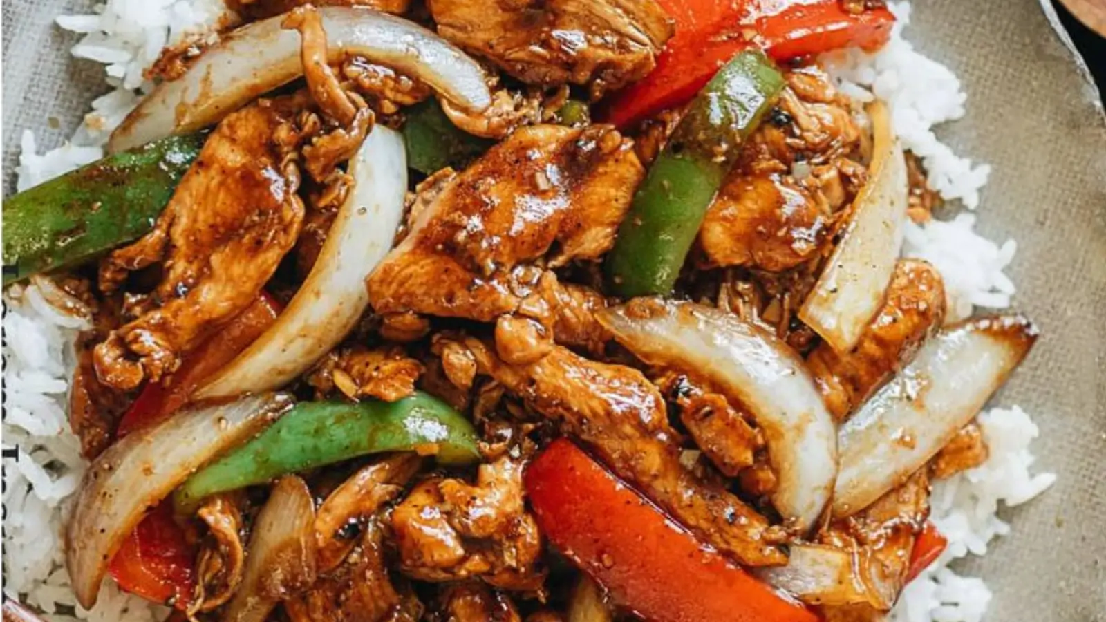 A plate of homemade Black Pepper Chicken stir-fry served over steamed white rice with tender chicken, onions, and red and green bell peppers in a savory black pepper sauce.