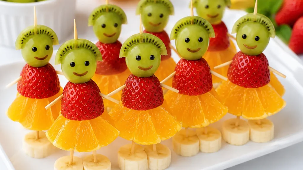 Cute fruit kabobs for kids made with grapes, kiwi slices, strawberries, orange slices, and banana pieces arranged as smiling fruit characters on a serving tray.