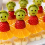 Cute fruit kabobs for kids made with grapes, kiwi slices, strawberries, orange slices, and banana pieces arranged as smiling fruit characters on a serving tray.